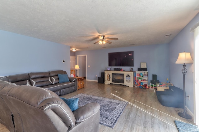 living room featuring a textured ceiling, a ceiling fan, baseboards, and wood finished floors