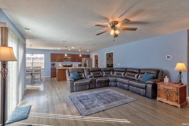 living area with visible vents, ceiling fan with notable chandelier, a textured ceiling, and light wood-type flooring