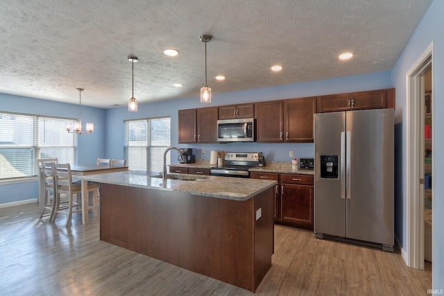 kitchen featuring a sink, appliances with stainless steel finishes, an island with sink, and light wood finished floors