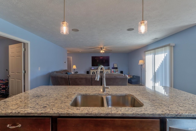 kitchen with hanging light fixtures, open floor plan, an island with sink, and a sink