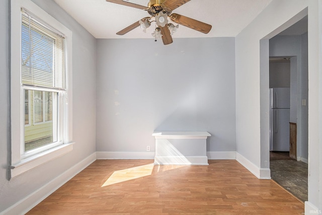 unfurnished room with baseboards, light wood-style floors, and a ceiling fan