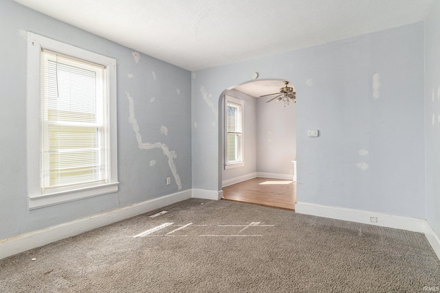 carpeted empty room with arched walkways, visible vents, a healthy amount of sunlight, and baseboards