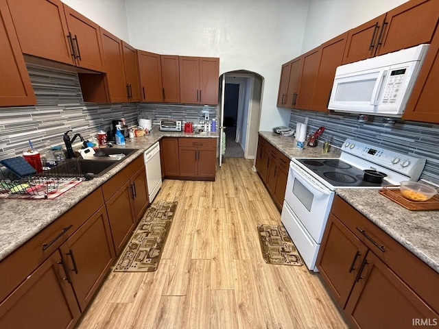 kitchen featuring white appliances, arched walkways, a sink, decorative backsplash, and light wood-type flooring