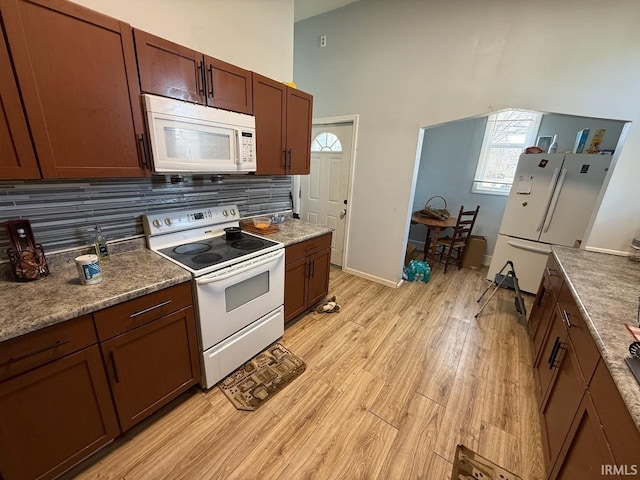 kitchen featuring light wood-style flooring, tasteful backsplash, white appliances, baseboards, and a towering ceiling