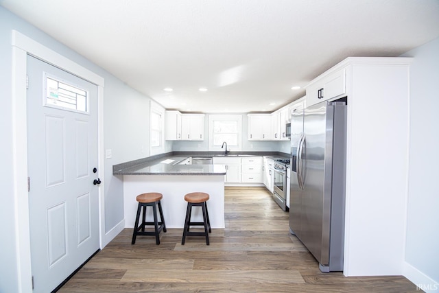 kitchen with dark countertops, wood finished floors, white cabinetry, stainless steel appliances, and a peninsula