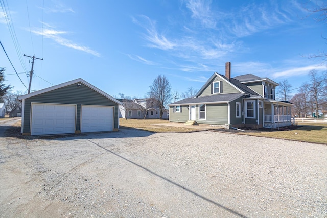 view of front of property with fence, covered porch, a chimney, a garage, and an outbuilding