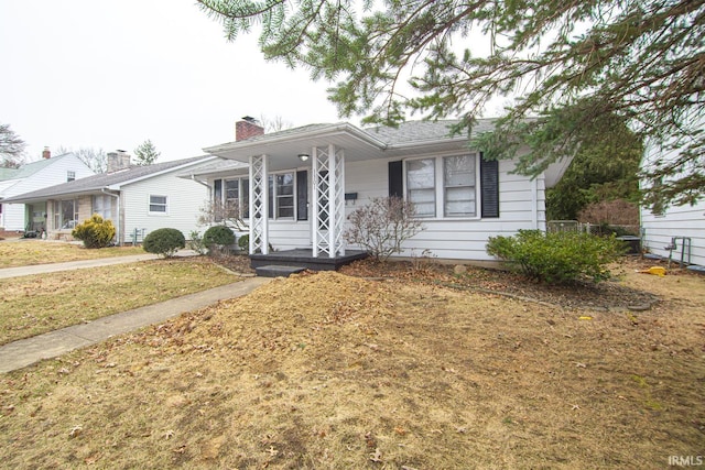 ranch-style home featuring a chimney, covered porch, and a front yard