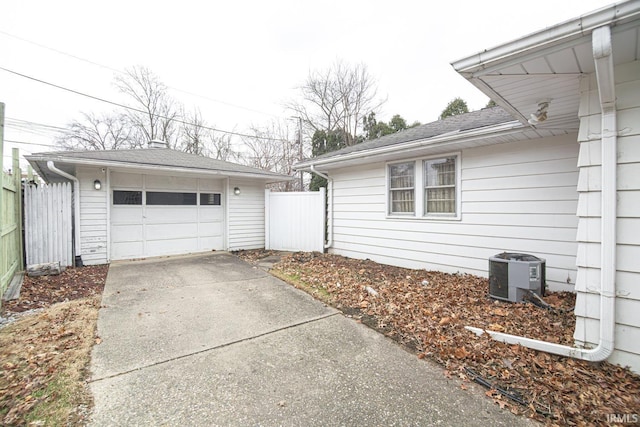 view of side of home featuring concrete driveway, central AC unit, fence, and an outbuilding