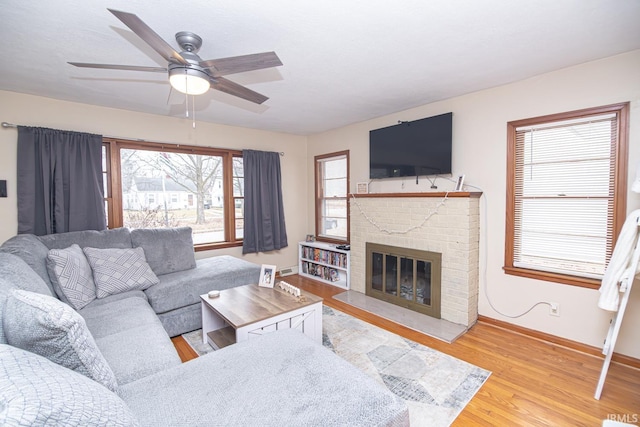 living area featuring a brick fireplace, wood finished floors, baseboards, and ceiling fan