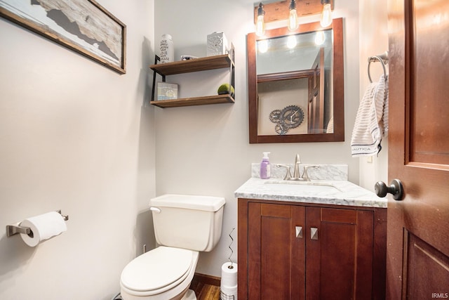 half bath featuring vanity, toilet, wood finished floors, and baseboards