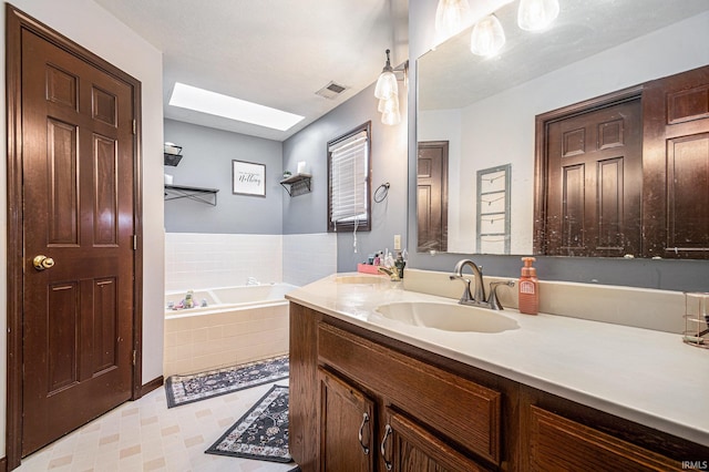 bathroom featuring tile patterned floors, visible vents, a garden tub, a skylight, and vanity