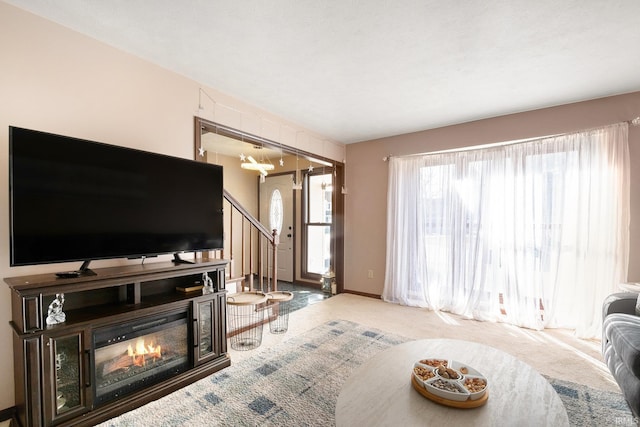 carpeted living room featuring a glass covered fireplace, stairs, and baseboards