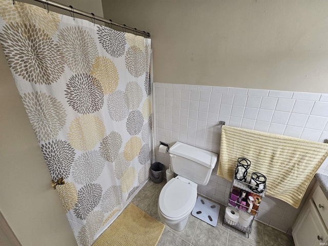 bathroom with toilet, a shower with shower curtain, tile walls, wainscoting, and tile patterned flooring