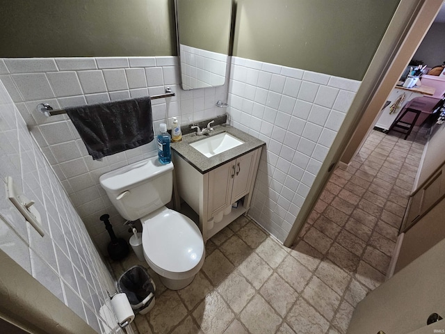 bathroom with tile walls, toilet, stone tile floors, and vanity