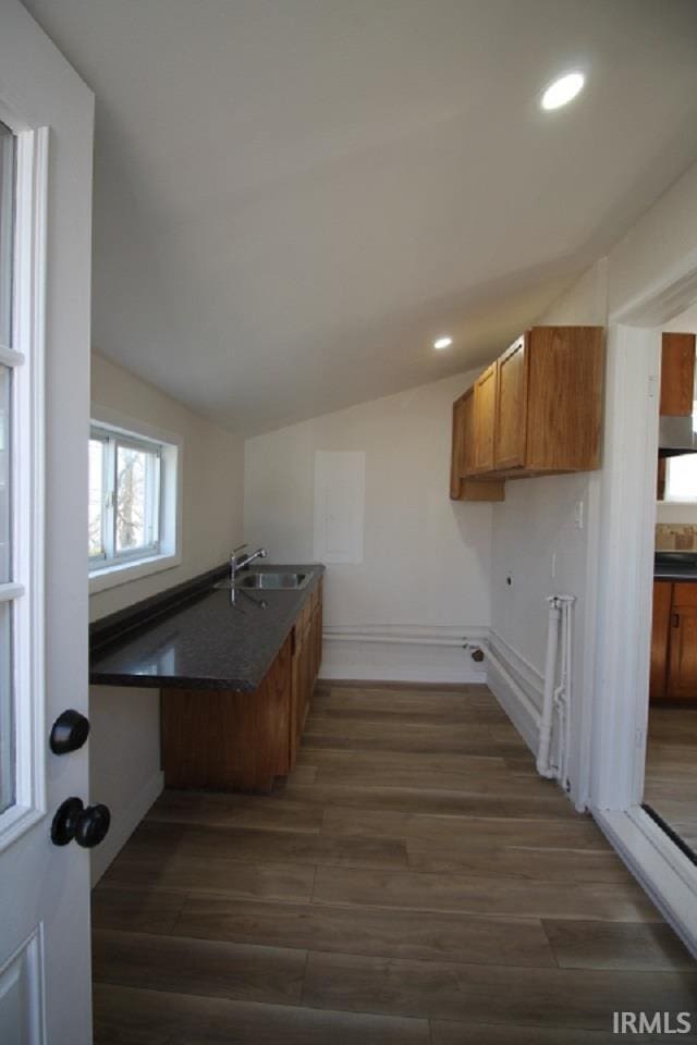 kitchen with brown cabinetry, lofted ceiling, dark wood-style flooring, a sink, and dark countertops