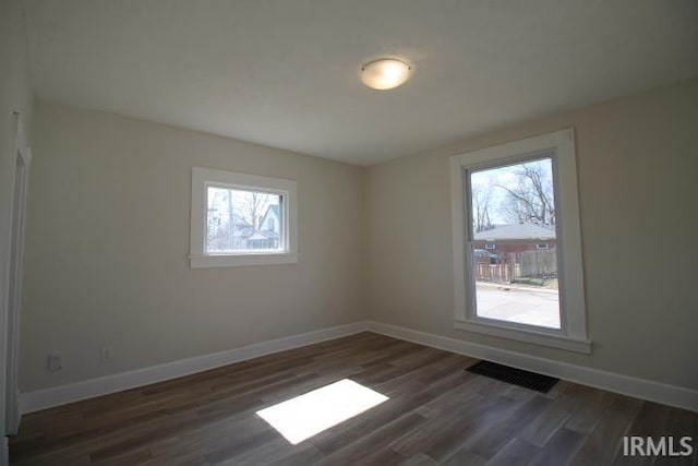 spare room with baseboards, visible vents, and dark wood-style flooring