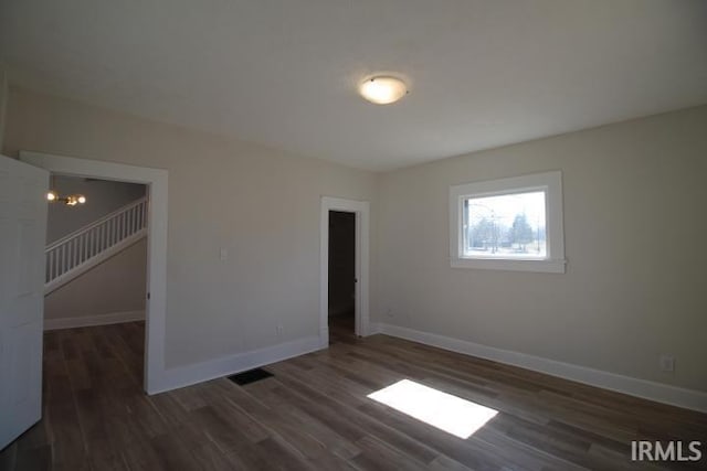 empty room with visible vents, baseboards, wood finished floors, and stairs