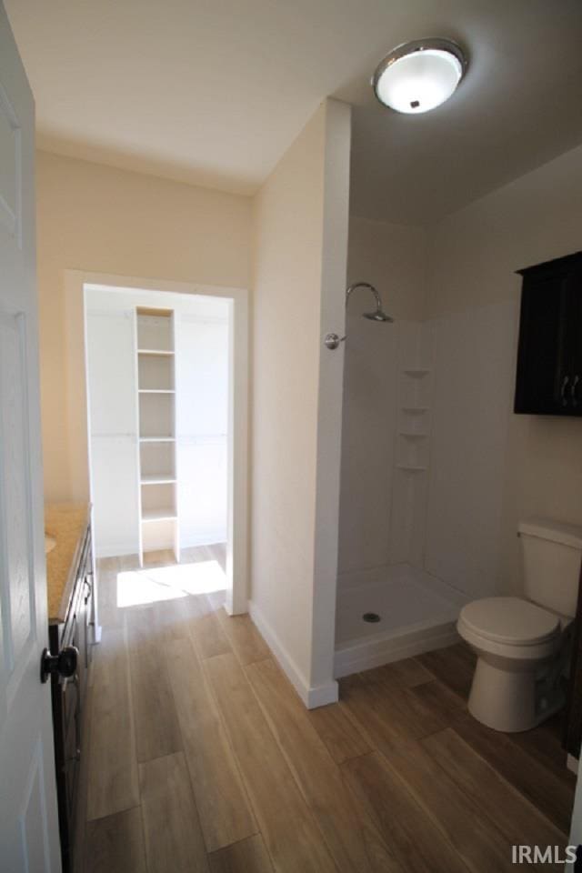 bathroom featuring toilet, wood finished floors, a shower, baseboards, and vanity