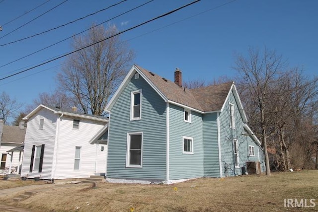 exterior space with a yard, roof with shingles, and a chimney