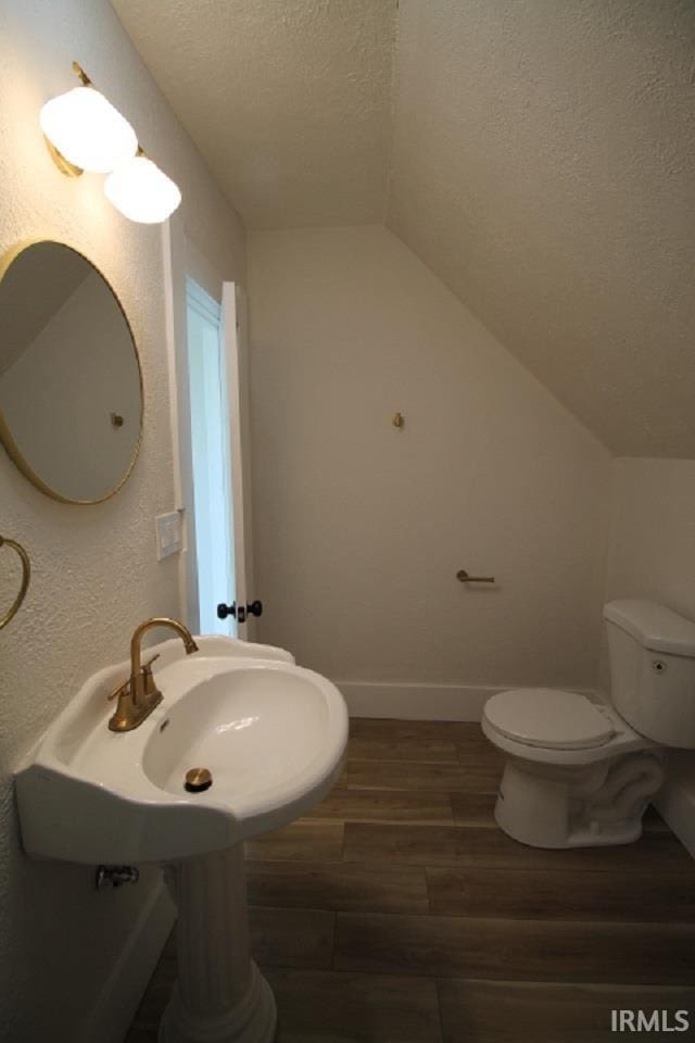 bathroom with baseboards, toilet, lofted ceiling, wood finished floors, and a textured ceiling