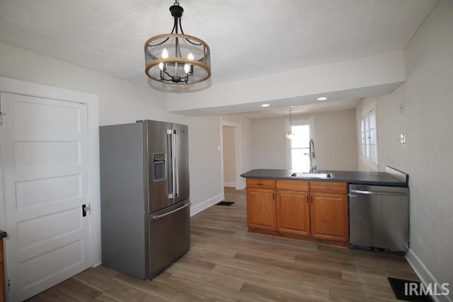 kitchen with brown cabinetry, appliances with stainless steel finishes, dark countertops, and wood finished floors