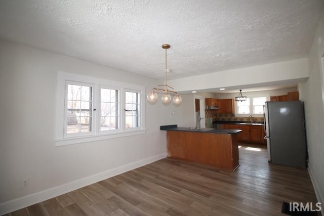 kitchen with a peninsula, dark wood-style flooring, freestanding refrigerator, dark countertops, and brown cabinets