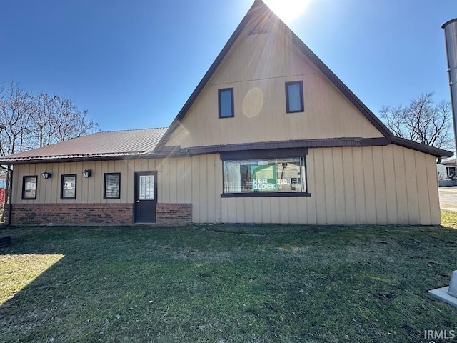 rear view of house featuring a yard, brick siding, and metal roof