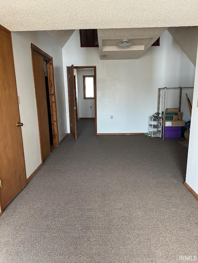 carpeted empty room with a textured ceiling, lofted ceiling, and baseboards