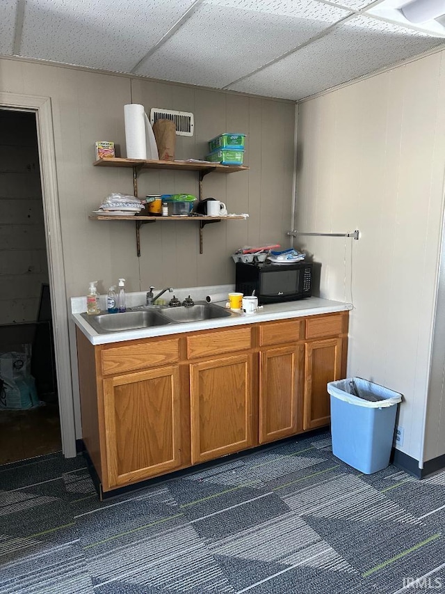 kitchen with a sink, black microwave, brown cabinetry, and light countertops