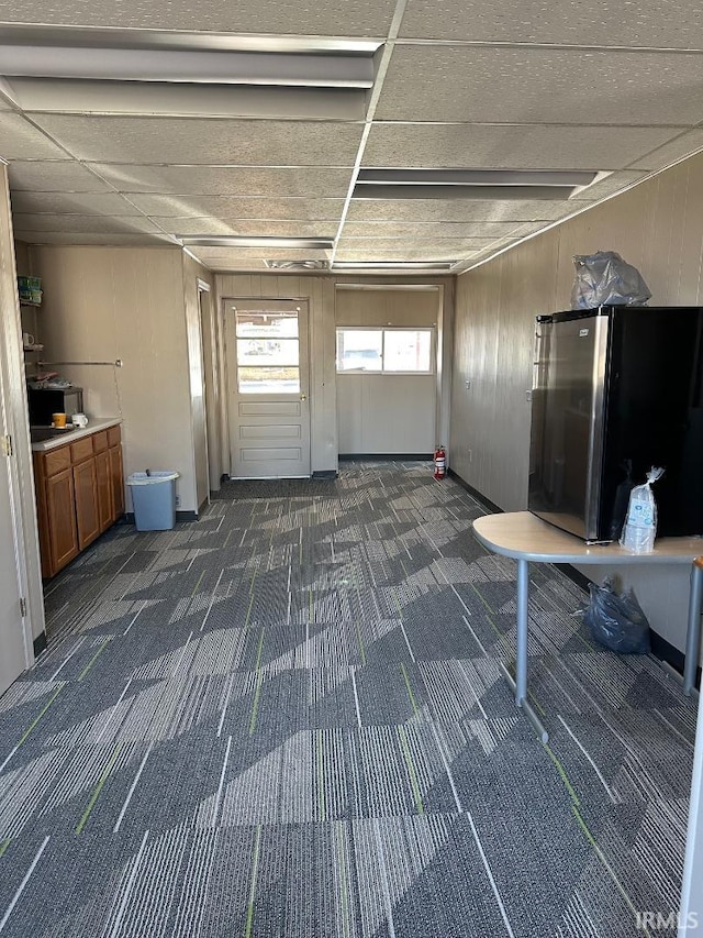 misc room with a garage, a paneled ceiling, dark colored carpet, and wood walls