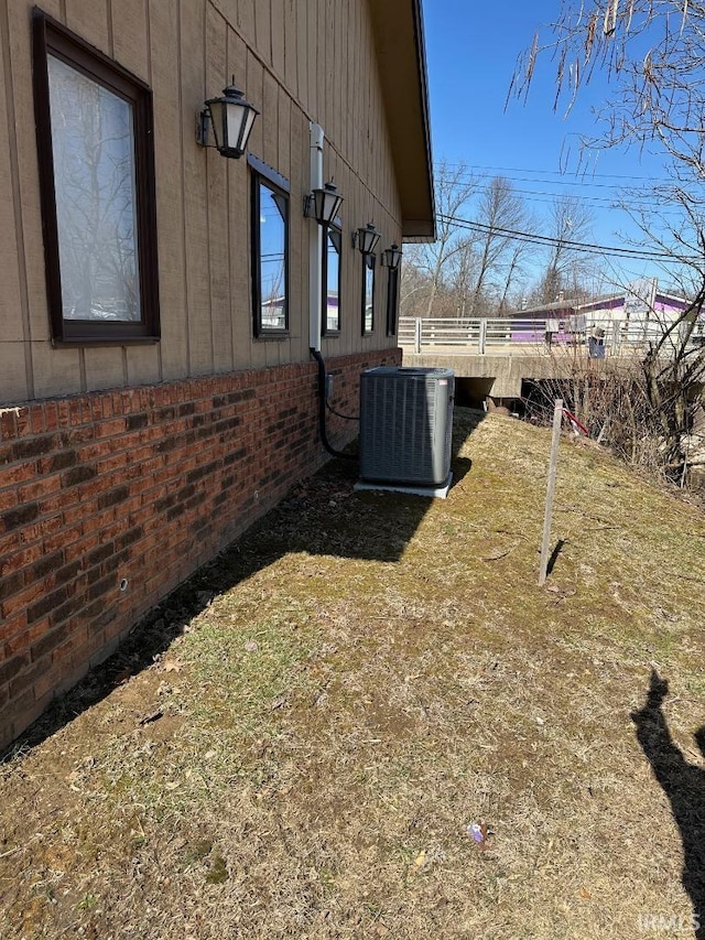 view of side of home with brick siding, central AC unit, and fence