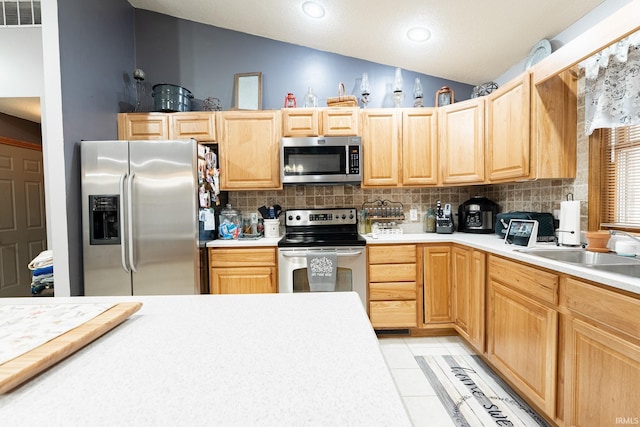 kitchen featuring visible vents, light brown cabinetry, vaulted ceiling, appliances with stainless steel finishes, and tasteful backsplash