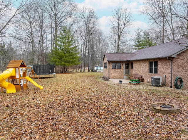 view of yard featuring central air condition unit, a playground, a trampoline, and an outdoor fire pit