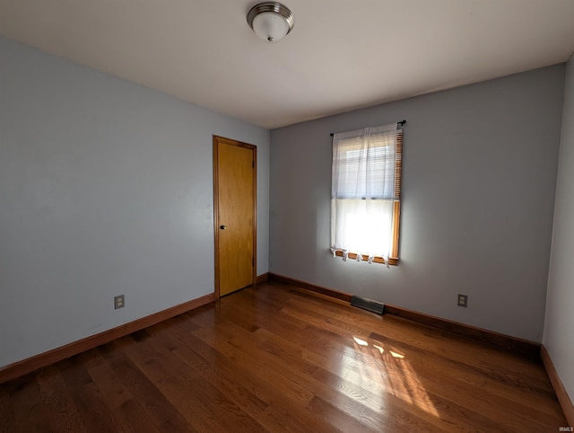 spare room with wood finished floors, visible vents, and baseboards