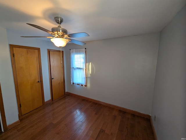 unfurnished bedroom with ceiling fan, baseboards, two closets, and wood finished floors