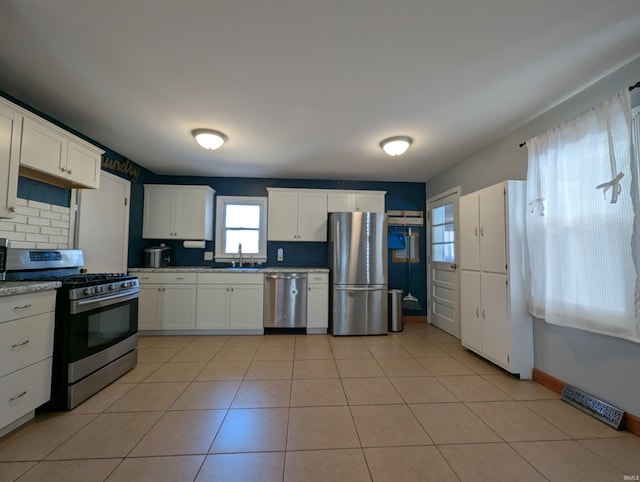 kitchen with a sink, white cabinets, light tile patterned flooring, and stainless steel appliances