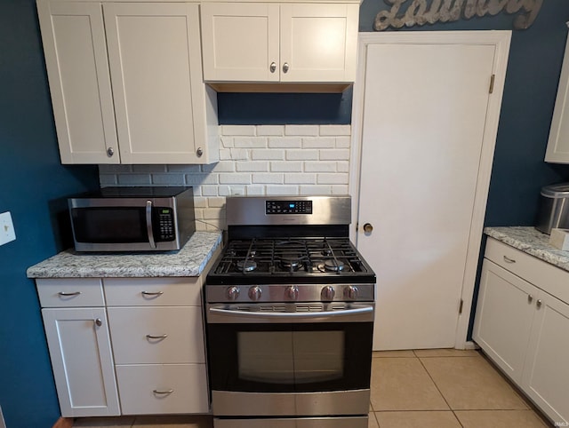 kitchen with light tile patterned flooring, backsplash, appliances with stainless steel finishes, and white cabinets