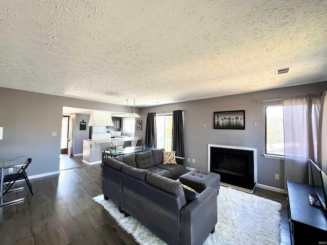 living area featuring dark wood-type flooring, a fireplace with raised hearth, baseboards, and visible vents