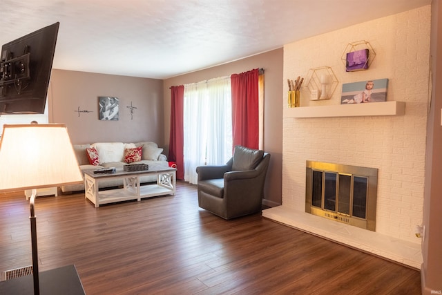 living area featuring a brick fireplace and dark wood-type flooring