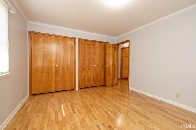 unfurnished bedroom with crown molding, light wood-style flooring, baseboards, and multiple closets