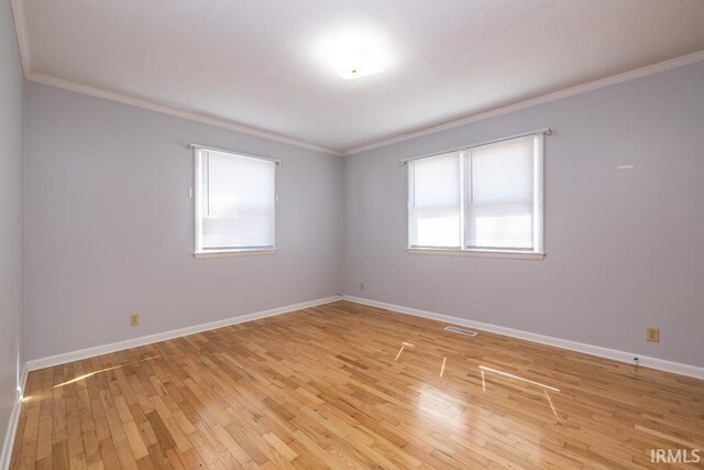 empty room with visible vents, crown molding, light wood-type flooring, and baseboards