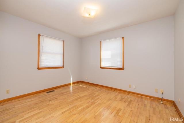 spare room featuring visible vents, light wood-style flooring, baseboards, and a healthy amount of sunlight