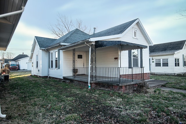 view of front of house featuring central air condition unit, roof with shingles, a porch, and a front yard