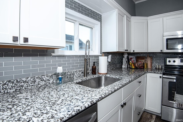 kitchen featuring light stone countertops, a sink, stainless steel appliances, white cabinets, and backsplash