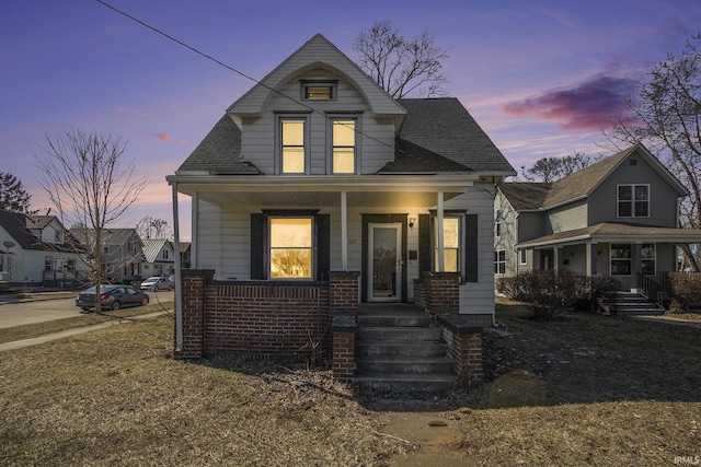 bungalow-style house with brick siding, covered porch, and roof with shingles