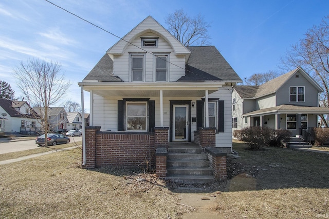 bungalow with brick siding, covered porch, and a shingled roof