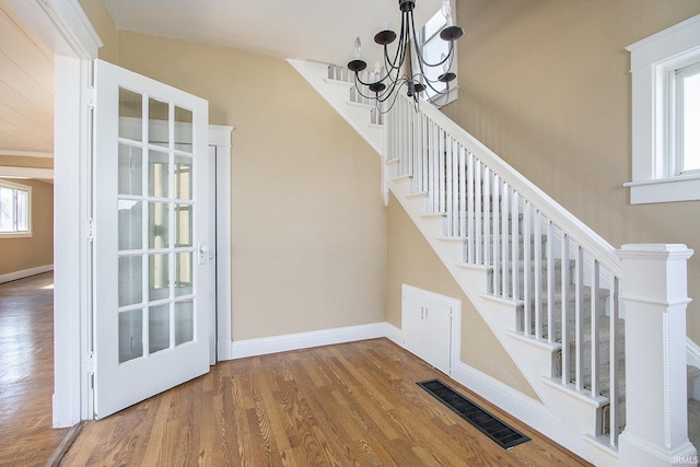 stairs featuring a notable chandelier, wood finished floors, visible vents, and baseboards