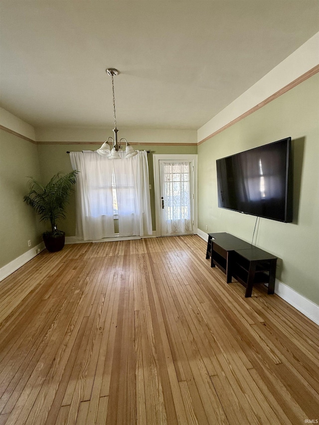 unfurnished living room with hardwood / wood-style flooring, baseboards, and a chandelier