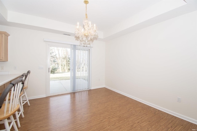 unfurnished dining area featuring a raised ceiling, wood finished floors, baseboards, and a chandelier