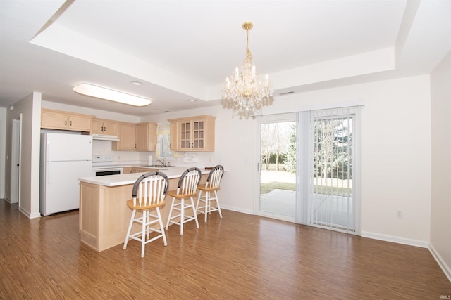 kitchen featuring light brown cabinetry, a tray ceiling, a peninsula, white appliances, and a sink